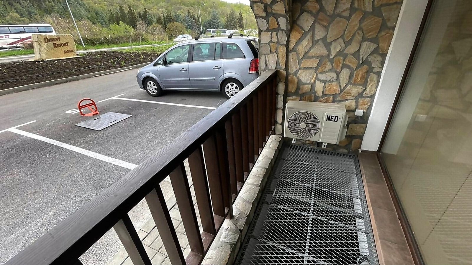 Балкон с решетчатым полом, кондиционером и видом на парковку с автомобилями, подходит для отдыха в Болгарии.