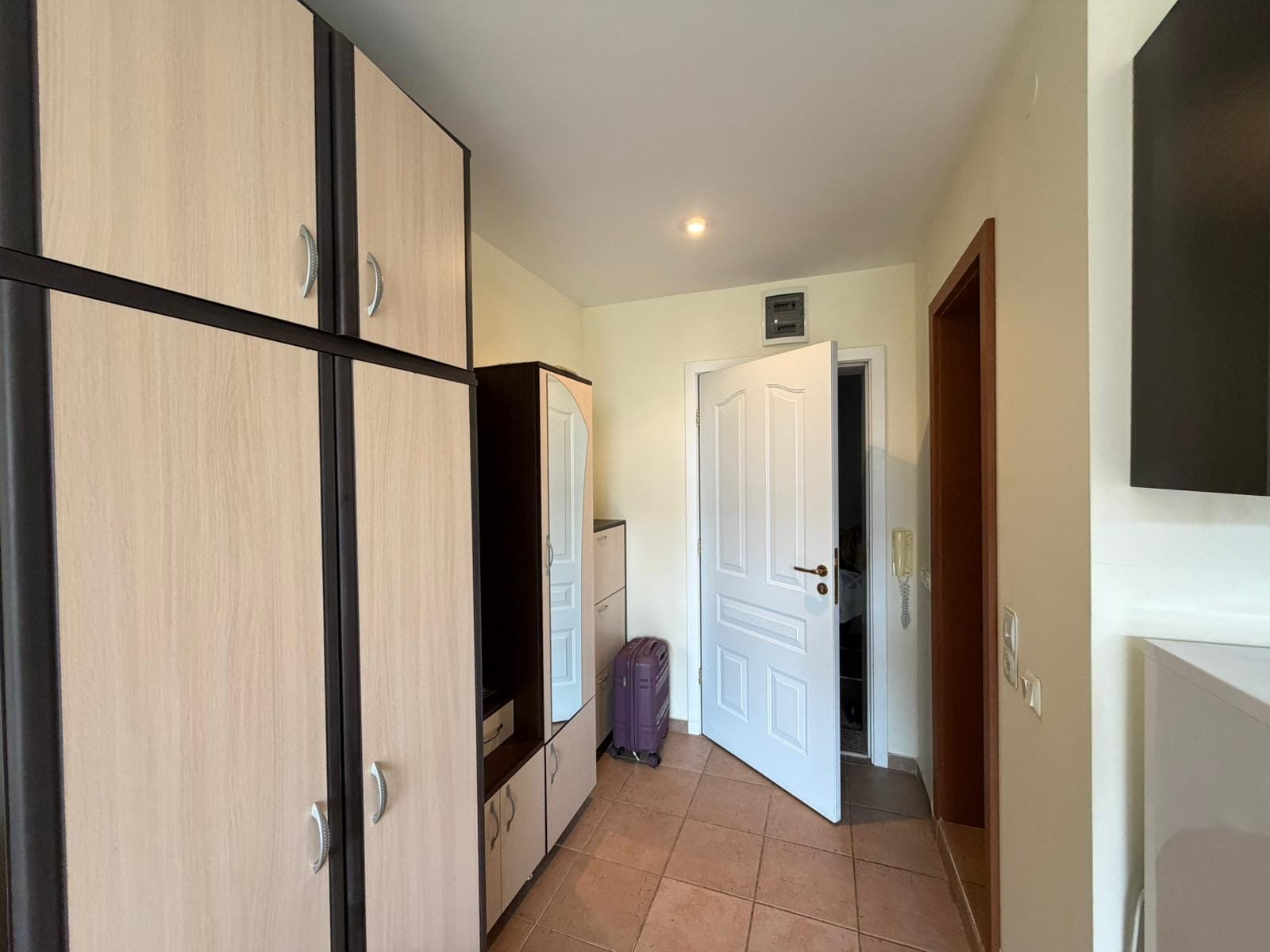 Современный интерьер прихожей с шкафом и открытой дверью. Современный коридор с встроенными шкафами и дверью, ведущей в квартиру для продажи в Болгарии.