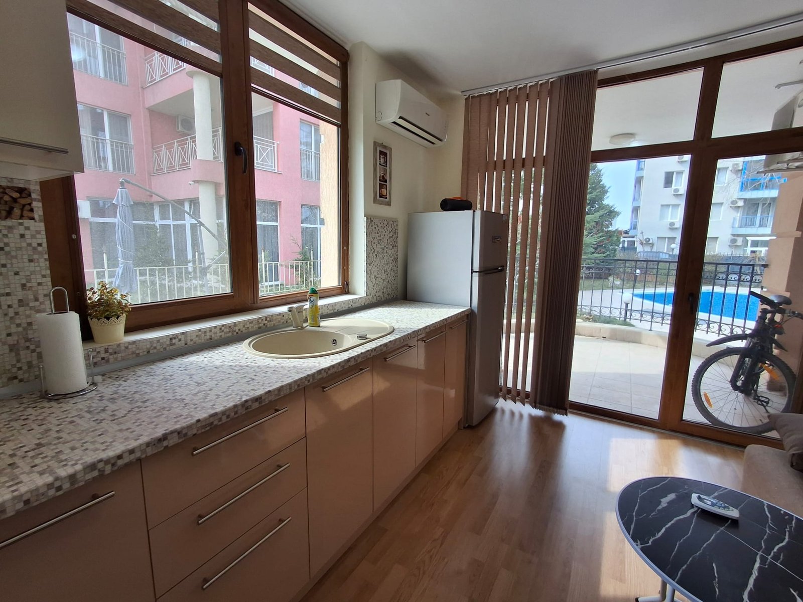 Современная кухня с открытой планировкой, стеклянными окнами, холодильником и видом на бассейн.