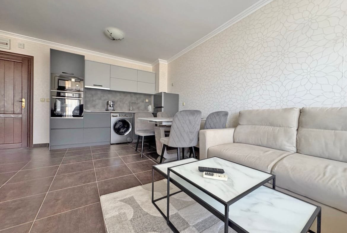 Современный интерьер квартиры с кухней и гостиной, серые стены, мягкий диван, обеденный стол и техника.