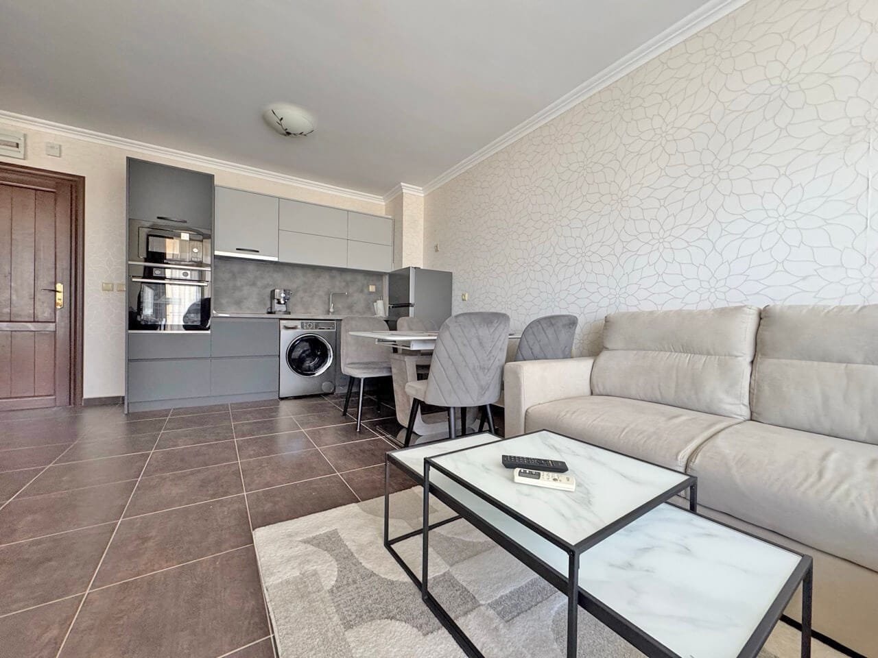 Современный интерьер квартиры: уютная кухня-гостиная в нейтральных тонах Современный интерьер квартиры с кухней и гостиной, серые стены, мягкий диван, обеденный стол и техника.