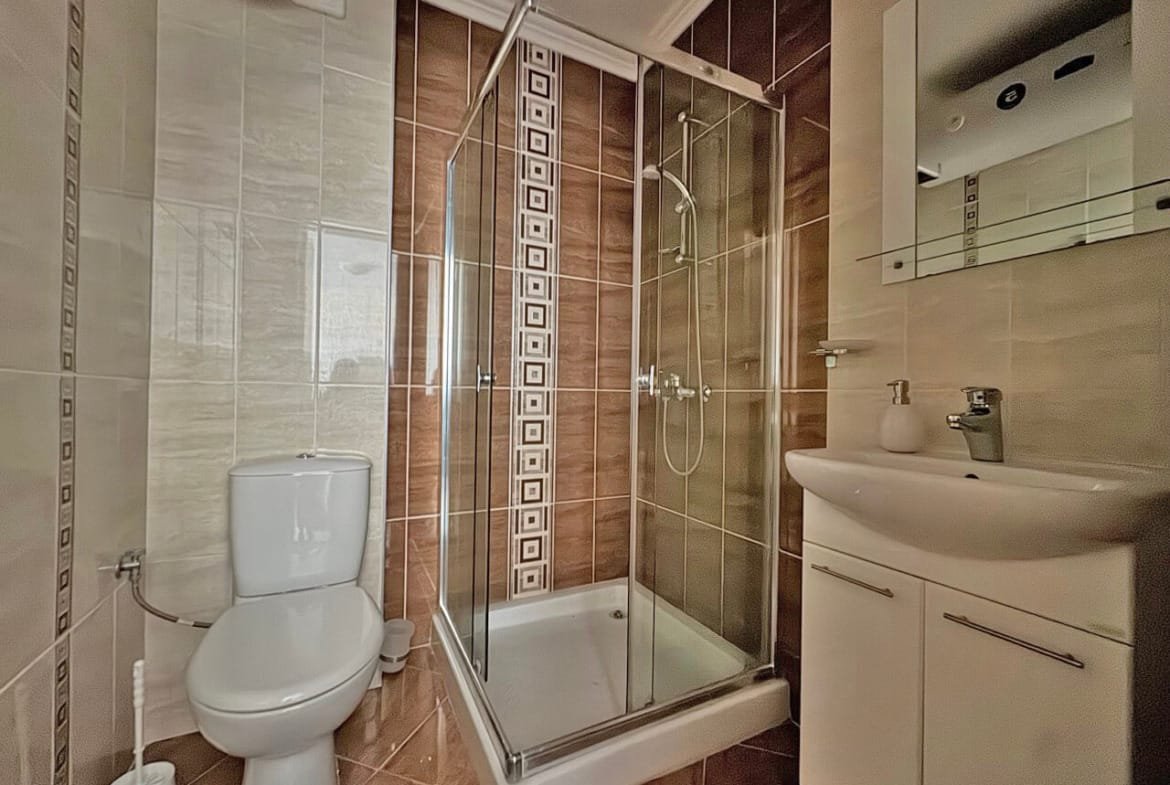 Современная ванная комната с душевой кабиной, унитазом и раковиной, оформленная в светлых и коричневых тонах.