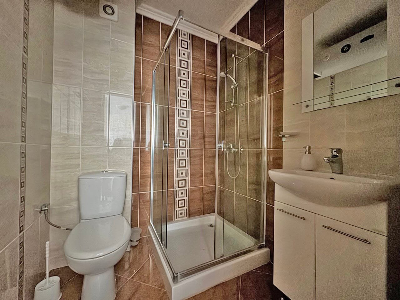 Современный санузел с душевой кабиной и стильным дизайном Современная ванная комната с душевой кабиной, унитазом и раковиной, оформленная в светлых и коричневых тонах.