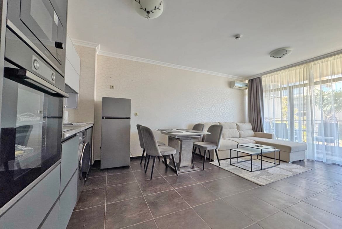 Современный светлый интерьер квартиры с кухней, обеденной зоной и уютной гостиной у окна с видом на улицу.