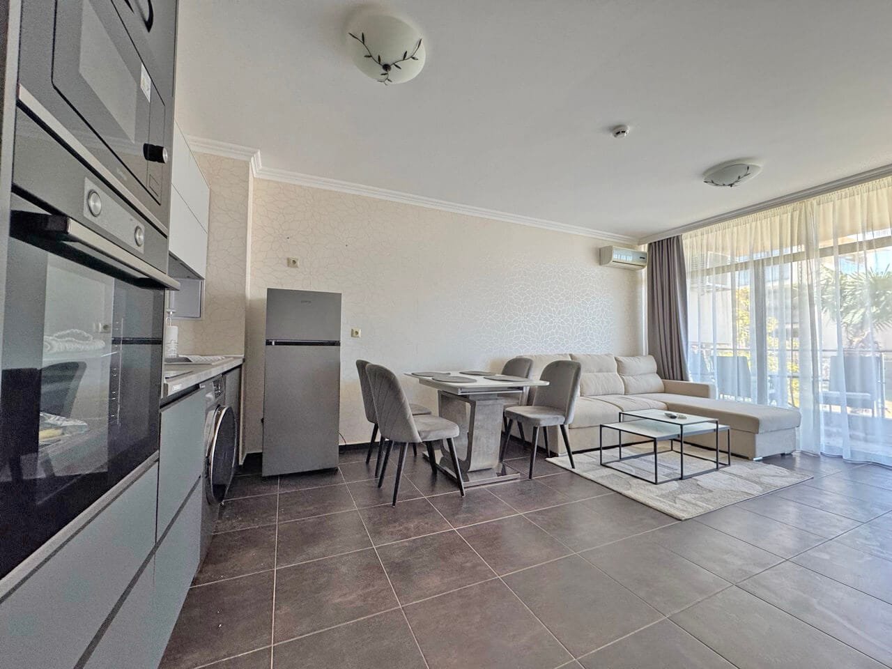 Современная квартира-студия с кухней и обеденной зоной Современный светлый интерьер квартиры с кухней, обеденной зоной и уютной гостиной у окна с видом на улицу.