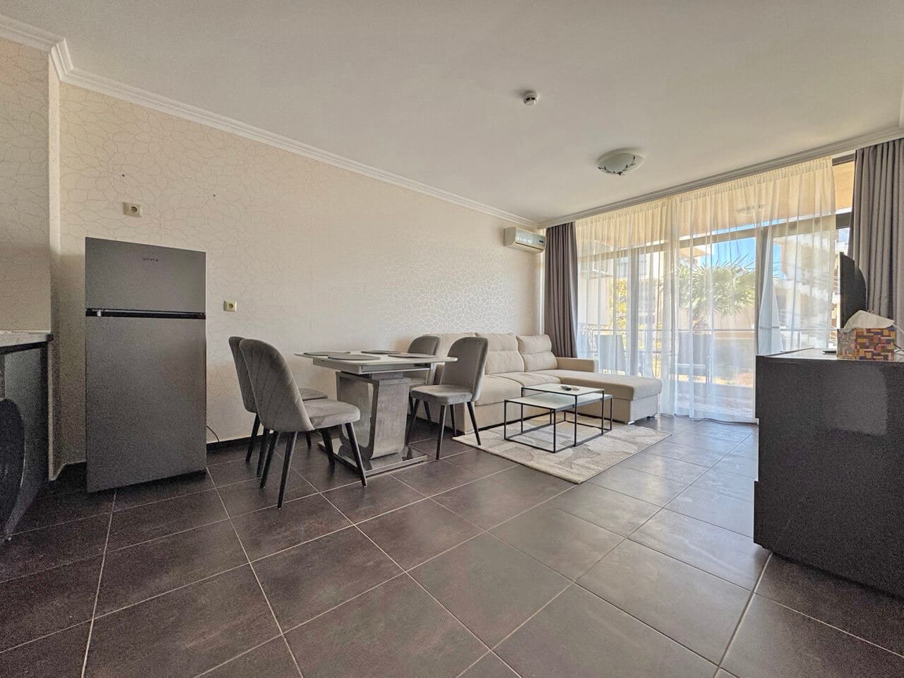 Современная гостиная с открытым пространством и мягкой мебелью Современный интерьер гостиной с светлыми стенами, мягким диваном, обеденным столом и большими окнами, пропускающими солнечный свет.