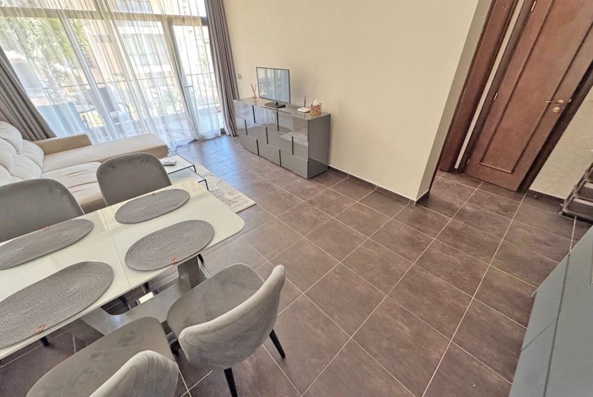 Современный интерьер квартиры с гостиной, телевизором и обеденным столом, оформленный в светлых и нейтральных тонах.