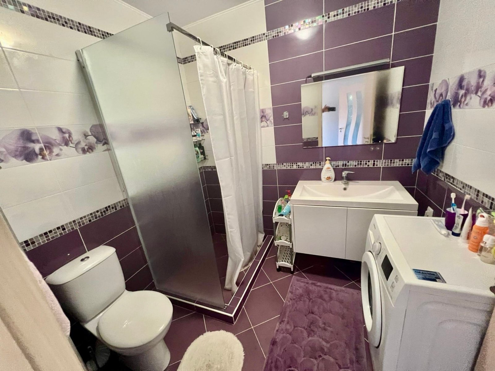 Современная ванная комната с душевой кабиной, умывальником и стиральной машиной, оформленная в фиолетовых и белых тонах.