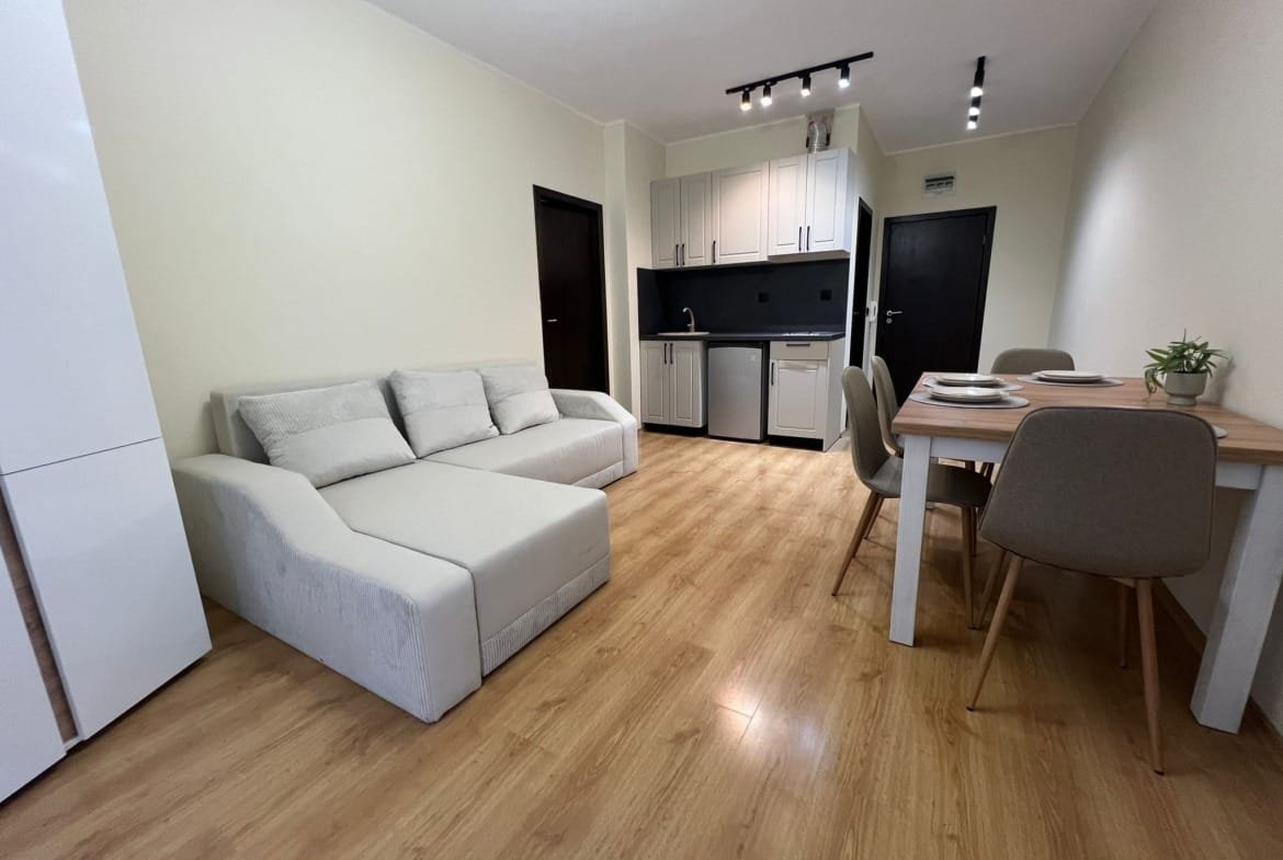 Современная кухня-студия с диваном и обеденным столом, оформленная в светлых тонах, идеальна для покупки недвижимости в Болгарии.