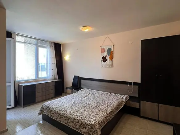 Современная спальня с двуспальной кроватью, комодом и шкафом, окна с видом на улицу, светлые тона интерьера.