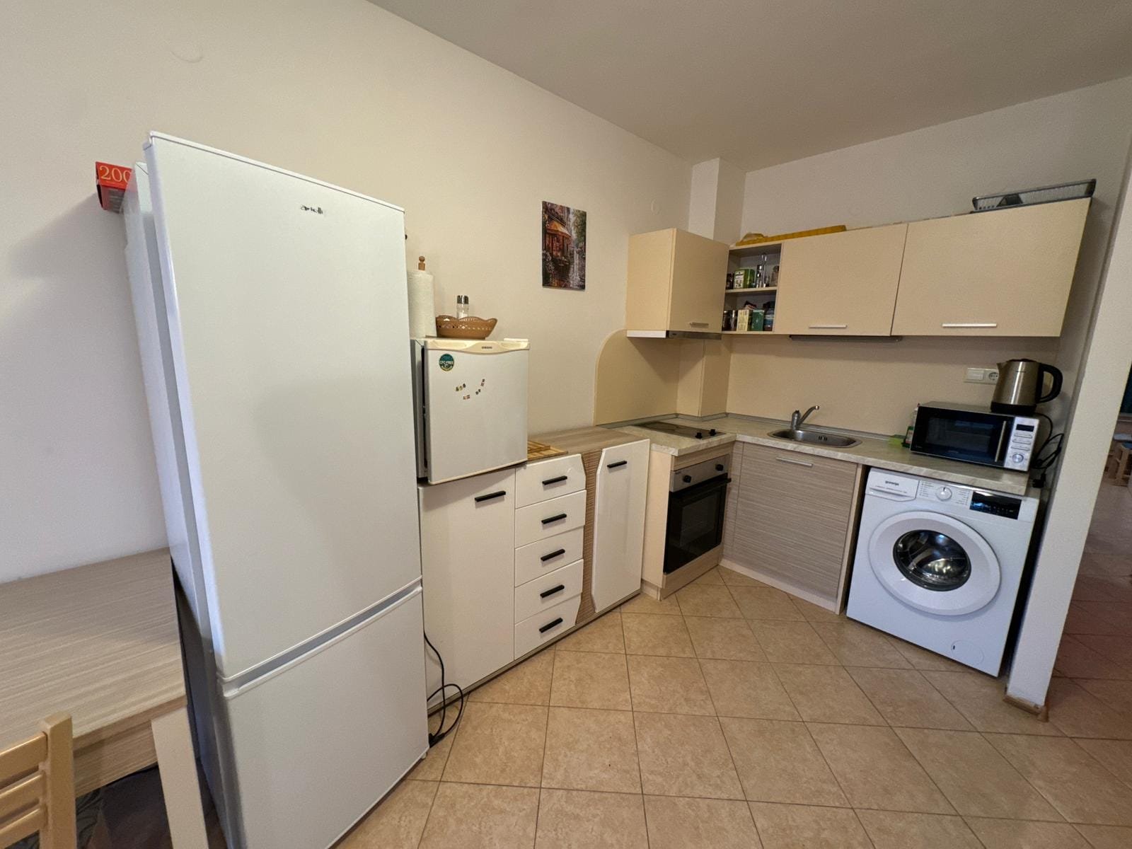 Современная кухня с бытовой техникой и обстановкой Современная кухня с белой техникой, столом, стульями и бытовыми приборами для комфортного проживания в Болгарии.