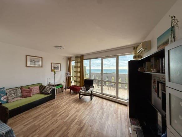 Современная гостиная с зелёным диваном и большим окном, предлагающим вид на море, подходит для жизни или аренды в Болгарии.