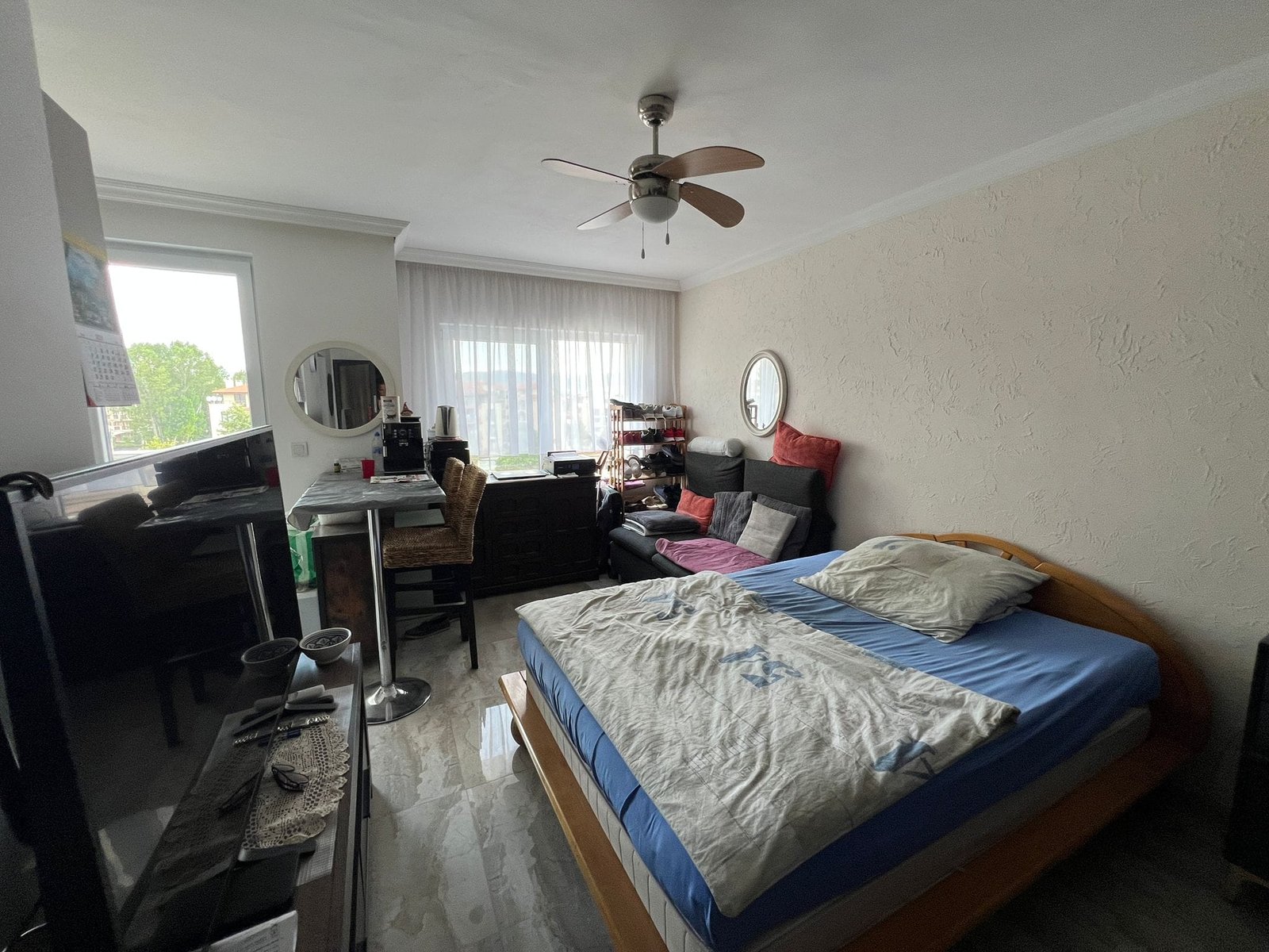 Уютная спальня с двуспальной кроватью, диваном и рабочим столом. Окно с видом на природу, мягкие тона интерьера.