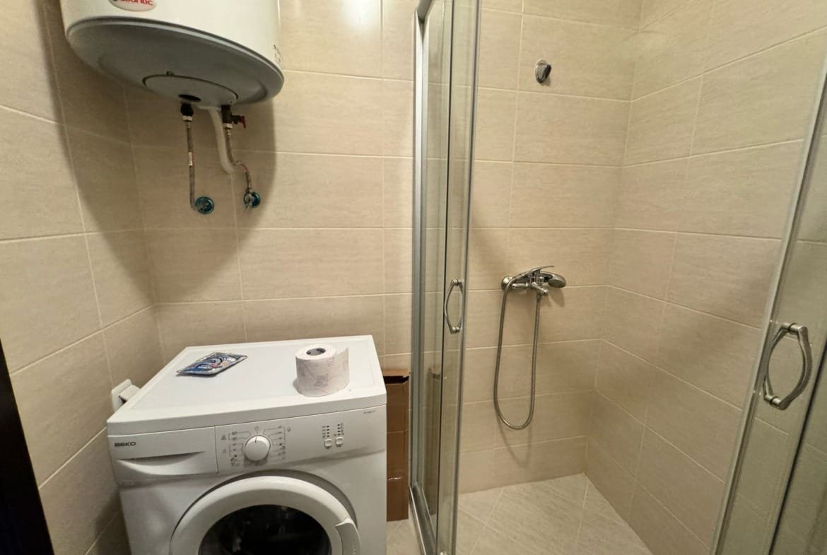 Современная ванная комната с душевой кабиной, стиральной машиной и встроенными аксессуарами для удобства в недвижимости Болгарии.