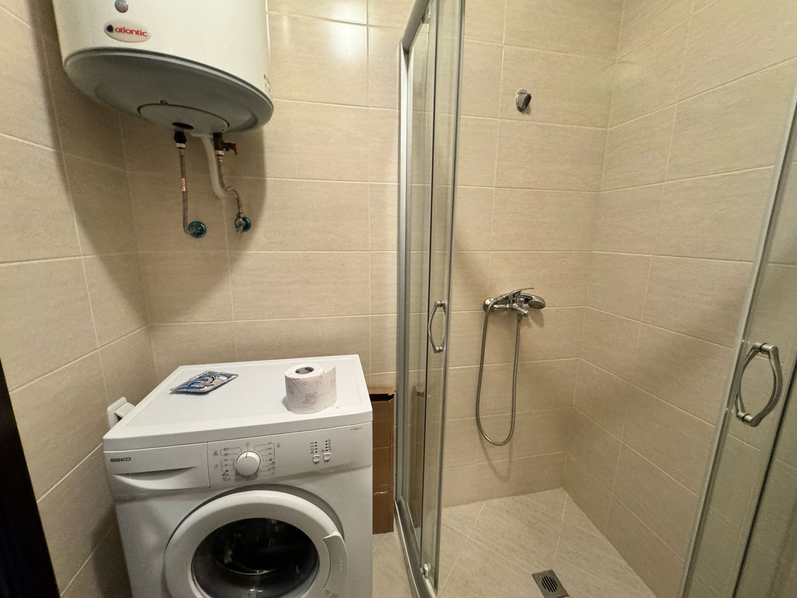 Современная ванная комната с душевой кабиной, стиральной машиной и встроенными аксессуарами для удобства в недвижимости Болгарии.