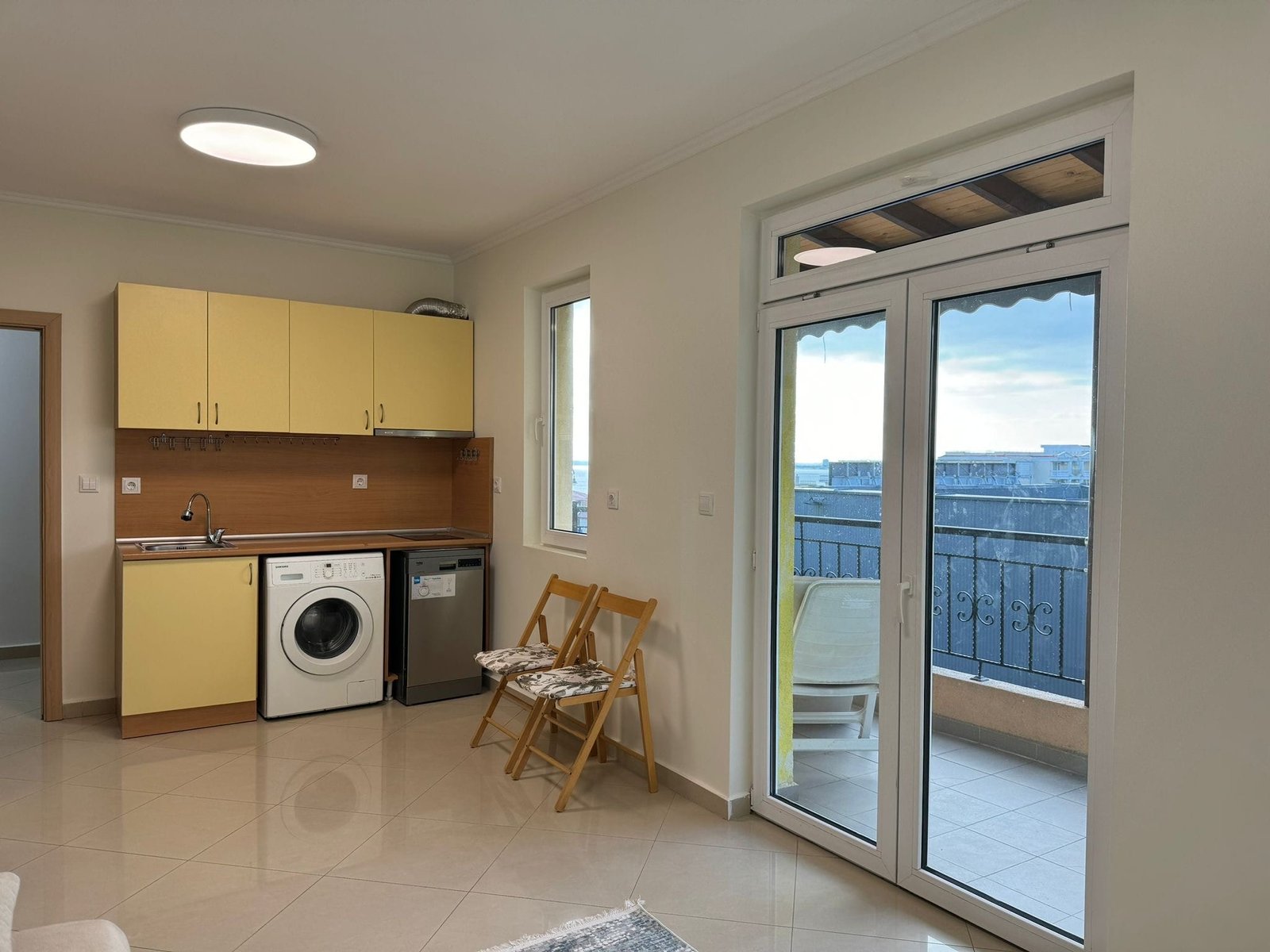 Современная кухня в квартире с балконом и стиральной машиной Современная кухня в квартире в Болгарии с бытовой техникой и выходом на балкон, идеальна для комфортной жизни и отдыха.