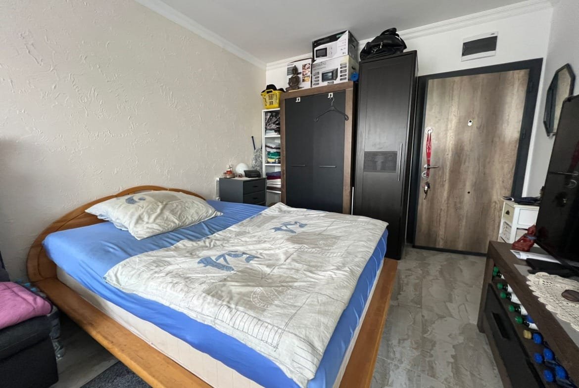 Современная спальня с двуспальной кроватью, шкафом и телевизором, подходит для комфортного проживания в Болгарии.