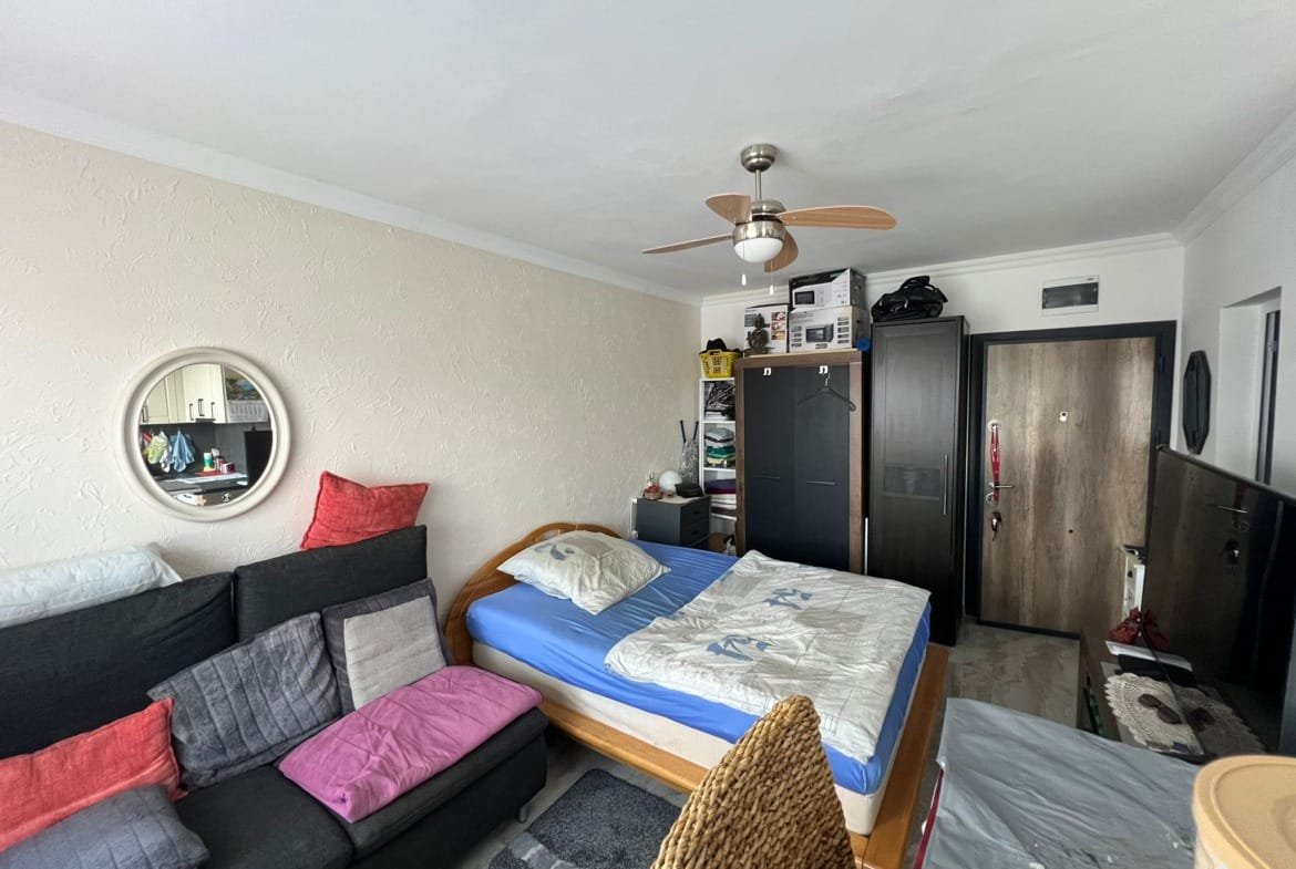 Уютная комната с кроватью, диваном и шкафом, оформленная в светлых тонах, идеально подходит для инвестиций в недвижимость в Болгарии.