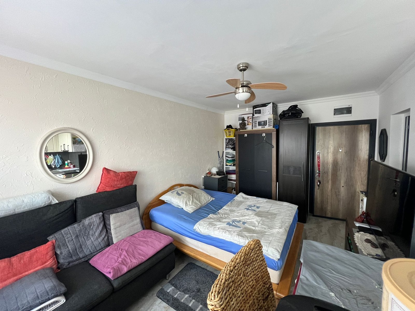 Уютная комната с кроватью, диваном и шкафом, оформленная в светлых тонах, идеально подходит для инвестиций в недвижимость в Болгарии.