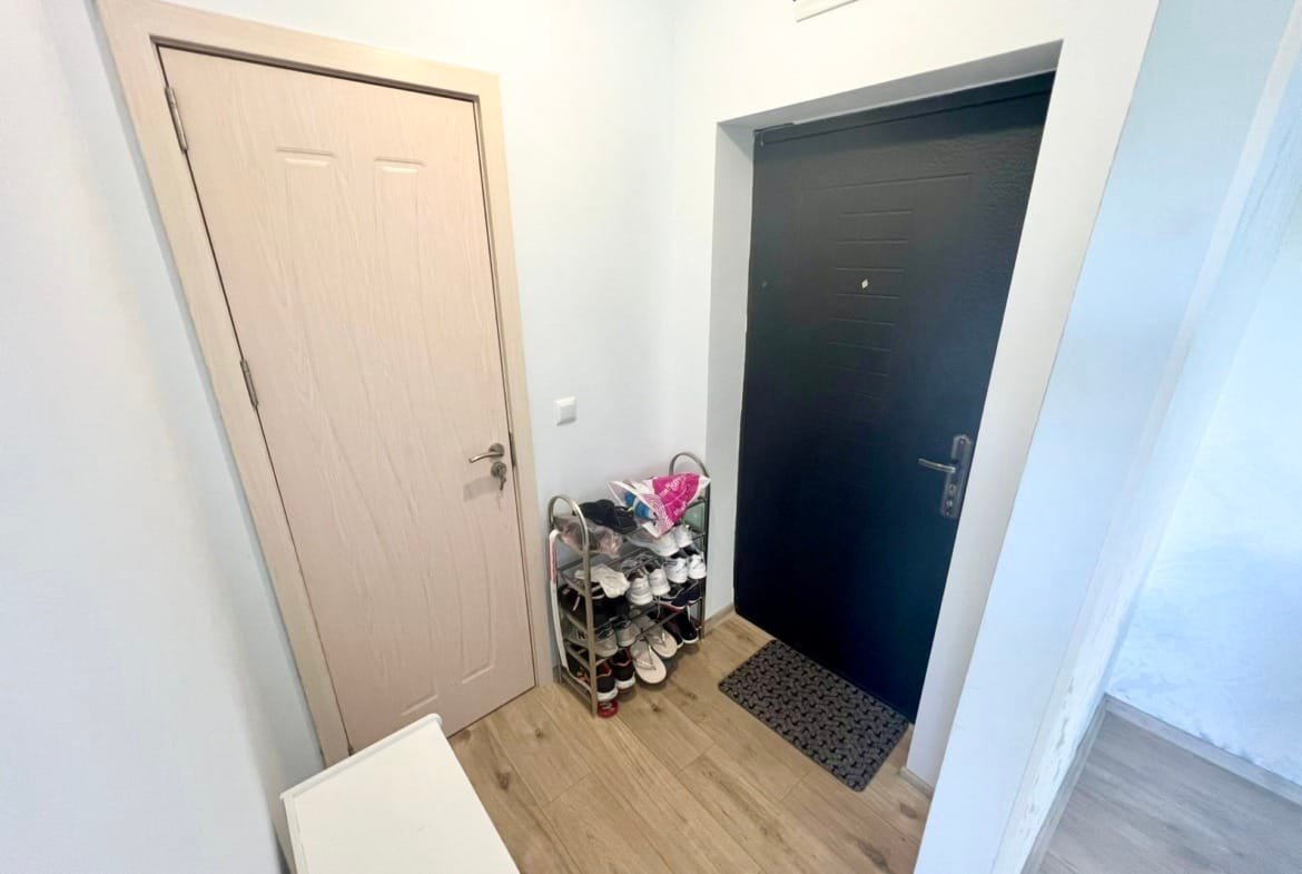 Современный входной коридор с черной дверью, обувницей и светлыми стенами, подходящий для покупки недвижимости в Болгарии.