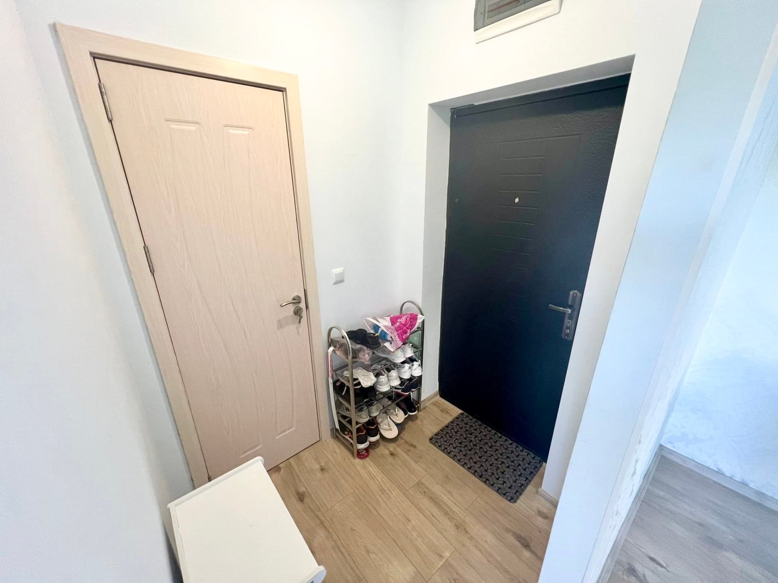 Современный входной коридор с черной дверью, обувницей и светлыми стенами, подходящий для покупки недвижимости в Болгарии.