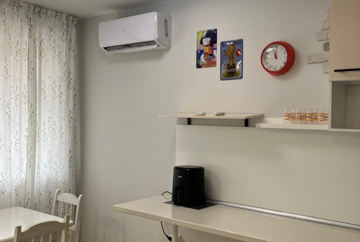 Современный интерьер квартиры с кухонным столом, кондиционером, часами и элементами декора в стиле минимализма.