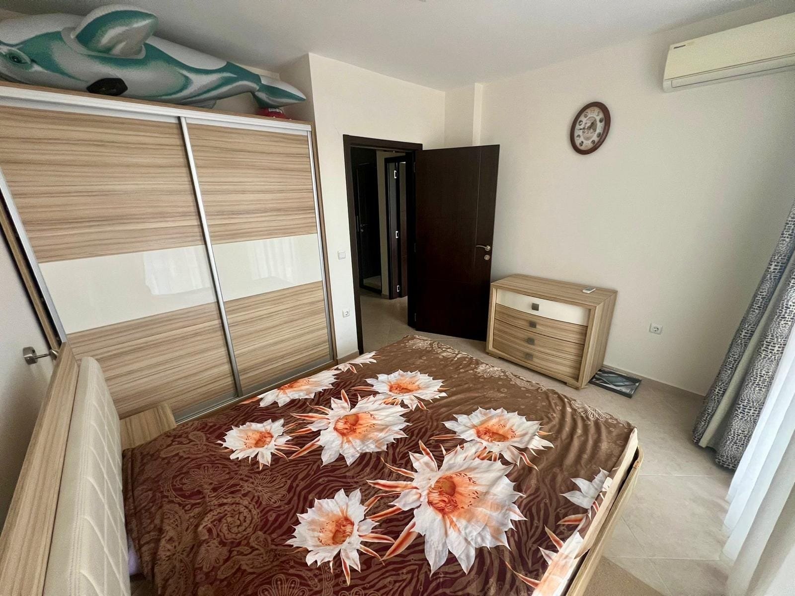 Современная спальня с двойной кроватью, шкафом, комодом и выходом на балкон, оформленная в светлых тонах для комфортного отдыха.