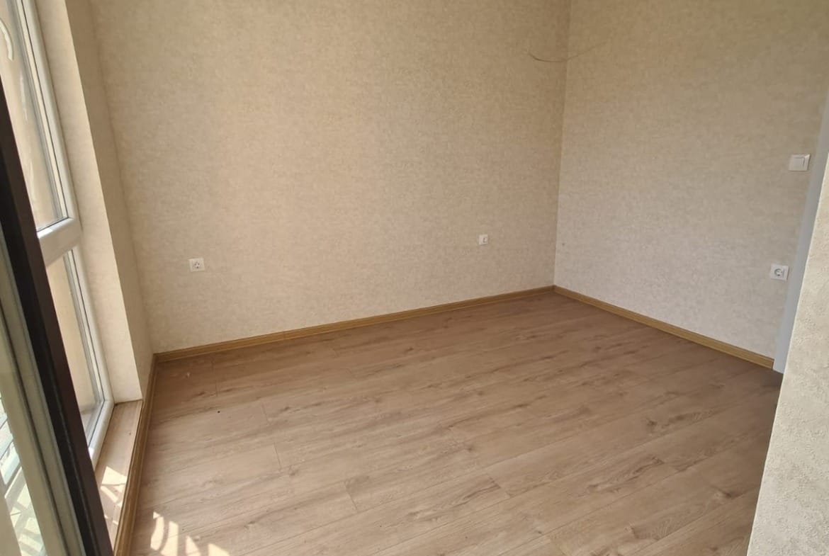 Светлая комната с деревянным полом и большими окнами, готовая для покупки или аренды недвижимости в Болгарии.