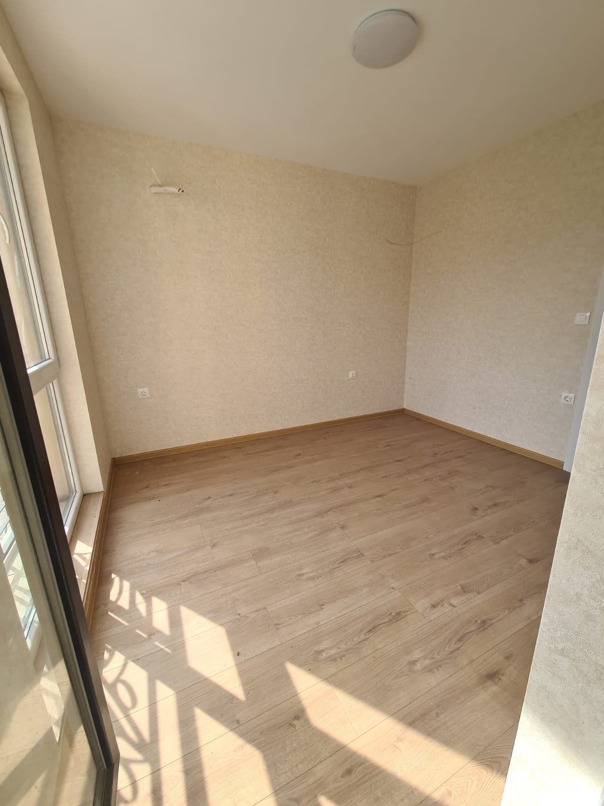 Светлая комната с деревянным полом и большими окнами, готовая для покупки или аренды недвижимости в Болгарии.