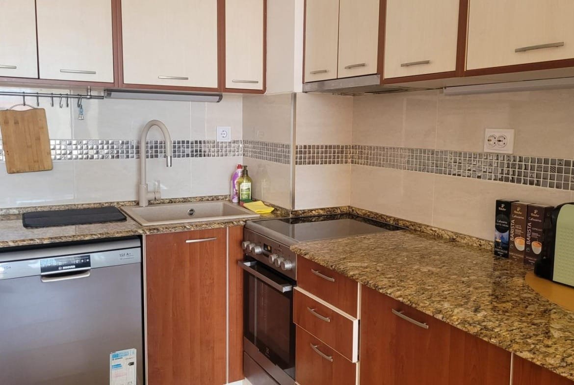 Современная кухня в Болгарии с гранитной столешницей, встроенной техникой и шкафами из светлого дерева. Идеально для покупки недвижимости.