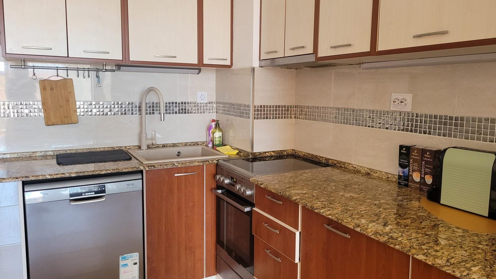 Современная кухня в Болгарии с гранитной столешницей, встроенной техникой и шкафами из светлого дерева. Идеально для покупки недвижимости.