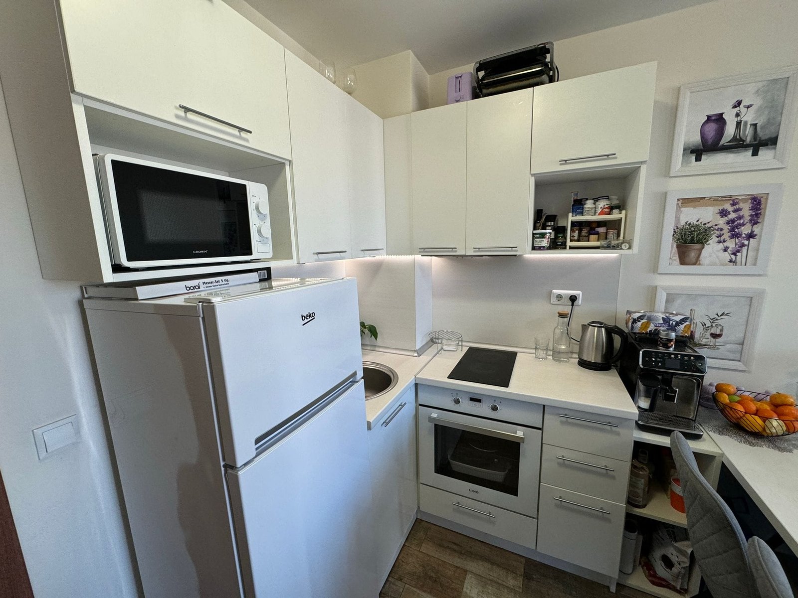 Современная кухня в светлых тонах с техникой и decor. Современная кухня с белыми шкафами, техникой, плитой и столешницей; идеальна для продажи и покупки недвижимости в Болгарии.