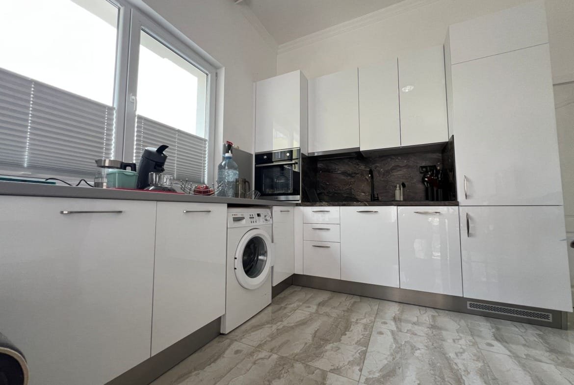 Современная кухня в квартире в Болгарии с белыми шкафами, стеклянными деталями и техникой для комфортного проживания.