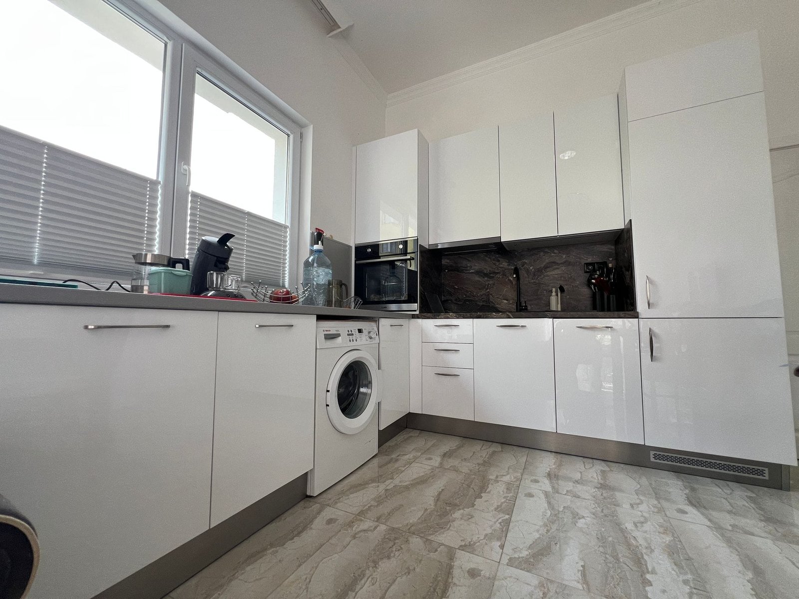 Современная кухня в квартире в Болгарии с белыми шкафами, стеклянными деталями и техникой для комфортного проживания.