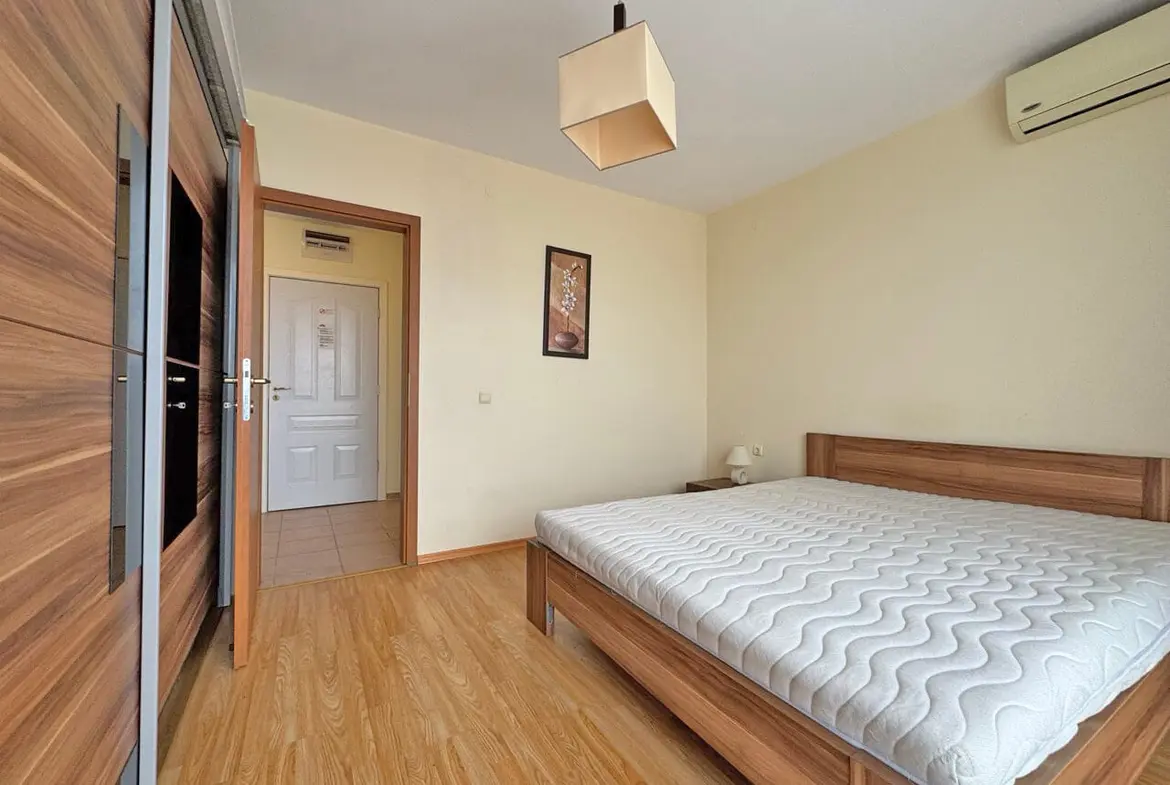 Современная спальня с деревянной мебелью, пустой кроватью и нейтральными стенами, освещенная естественным светом.