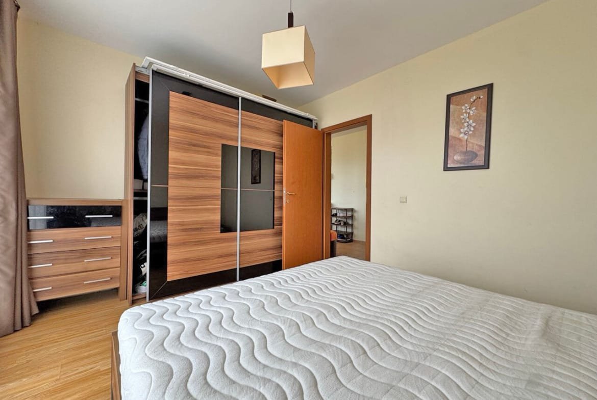 Современная спальня с кроватью, шкафом с зеркальными дверцами и лампой, стены светлого цвета, паркетный пол.