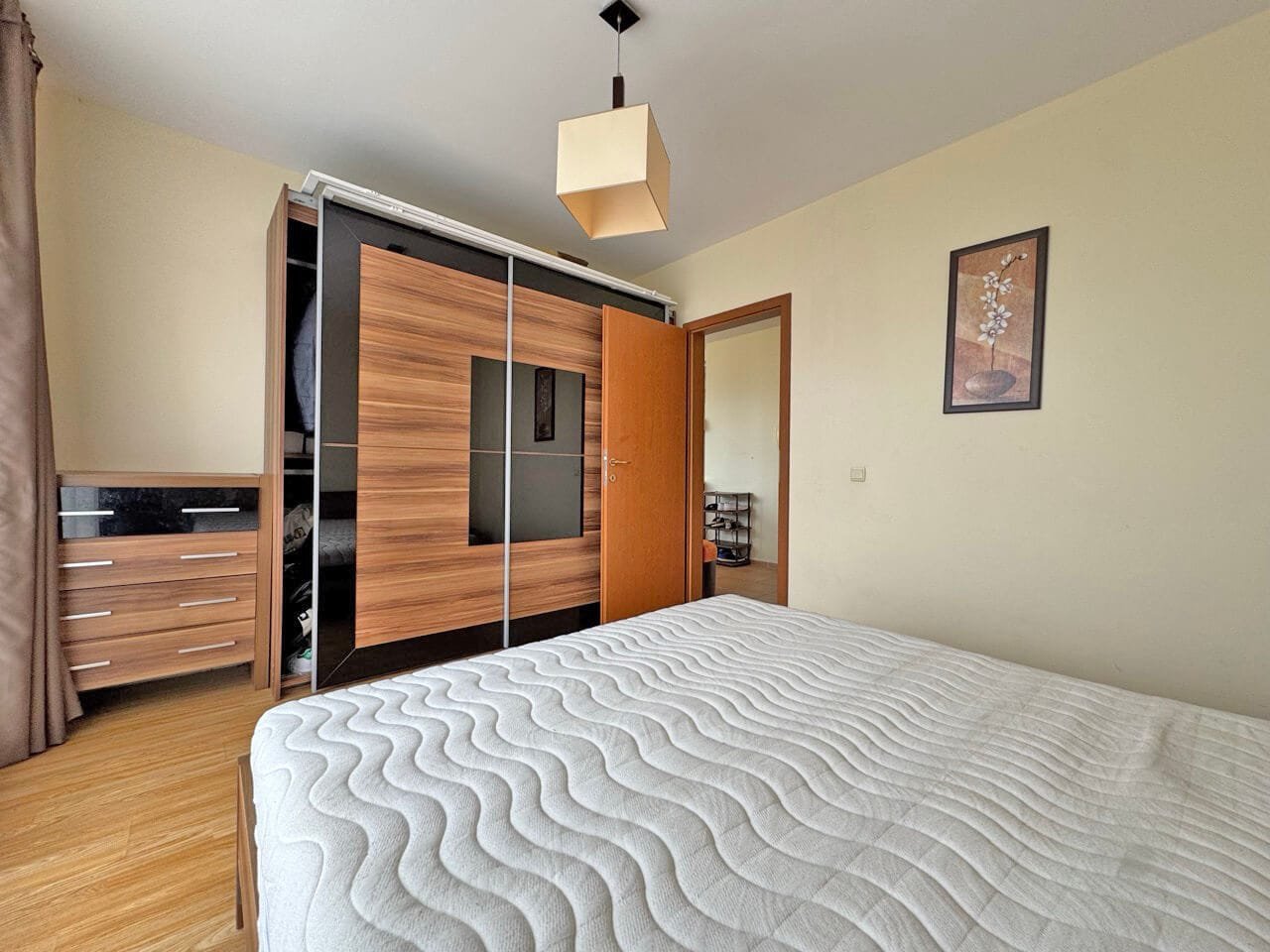 Современная спальня с кроватью, шкафом с зеркальными дверцами и лампой, стены светлого цвета, паркетный пол.