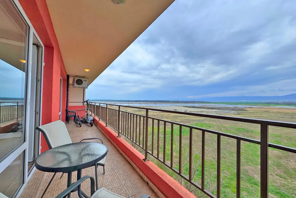 Балкон с круглыми столом и стульями, открывающий вид на облачное небо и зелёный ландшафт.