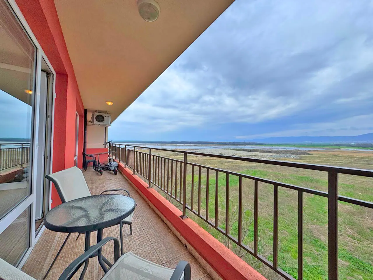 Балкон с круглыми столом и стульями, открывающий вид на облачное небо и зелёный ландшафт.