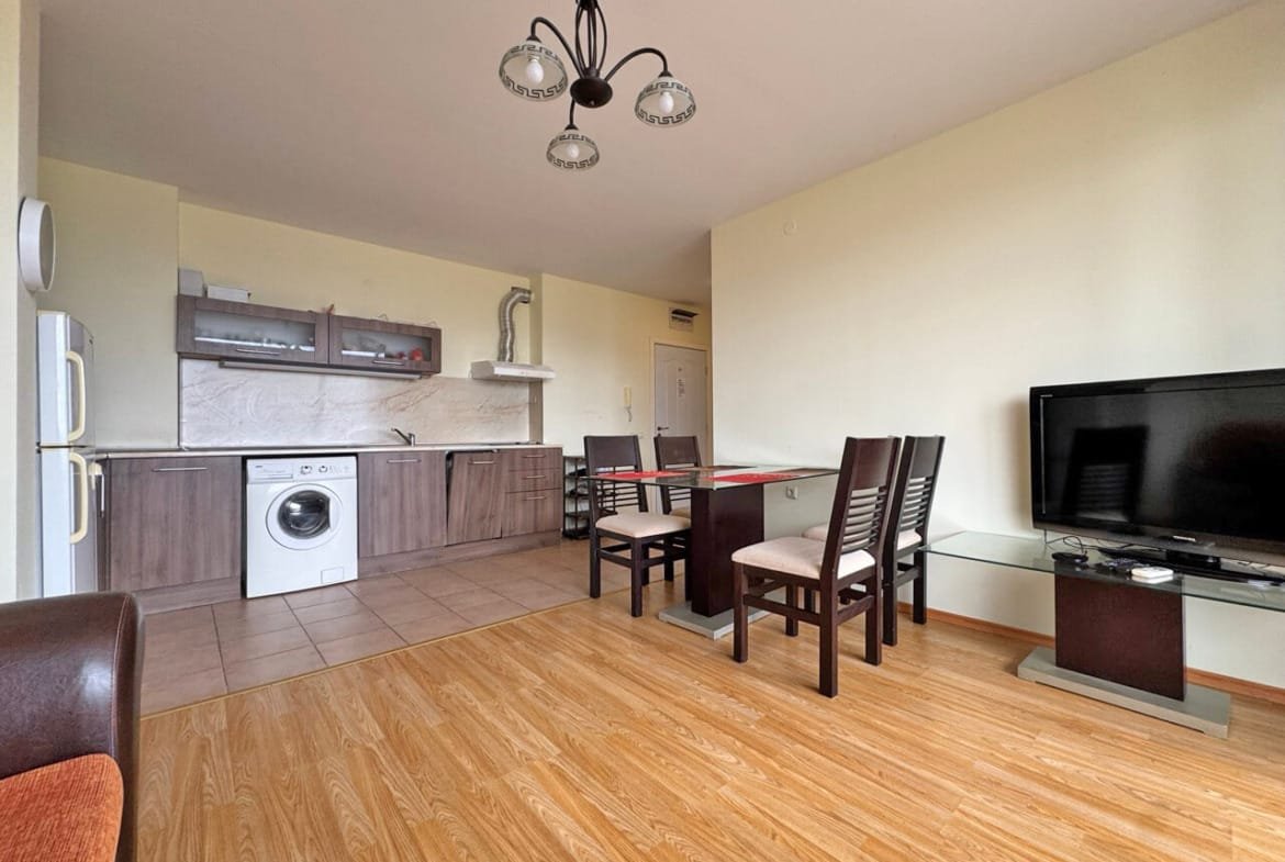 Современная кухня-студия с обеденной зоной, стиральной машиной и телевизором, отделка в нейтральных тонах.