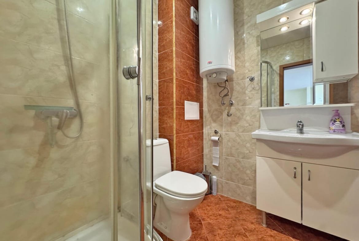 Современная ванная комната с душевой кабинкой, унитазом и раковиной на фоне светлых и тёмных плиток.