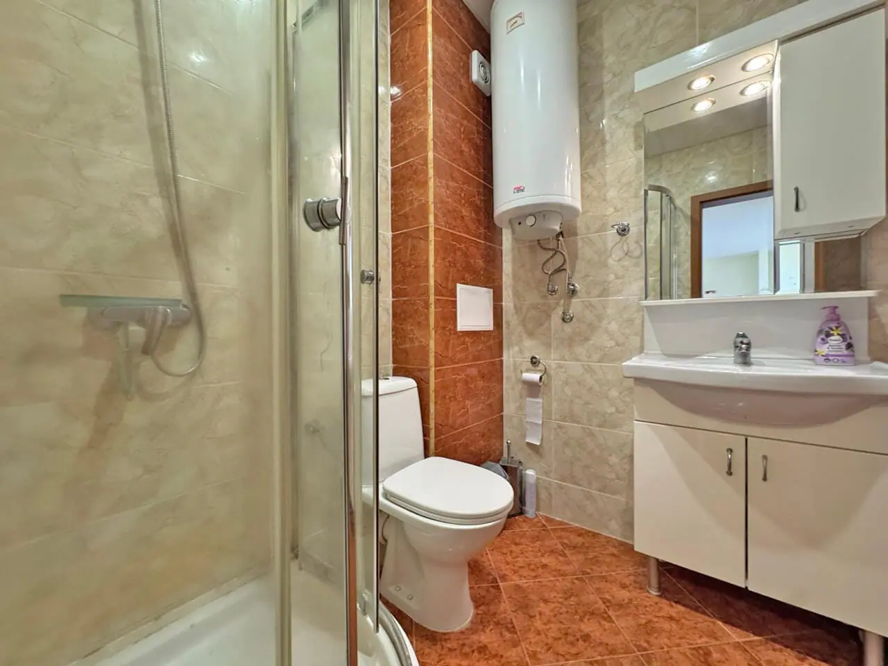 Современная ванная комната с душевой кабинкой, унитазом и раковиной на фоне светлых и тёмных плиток.