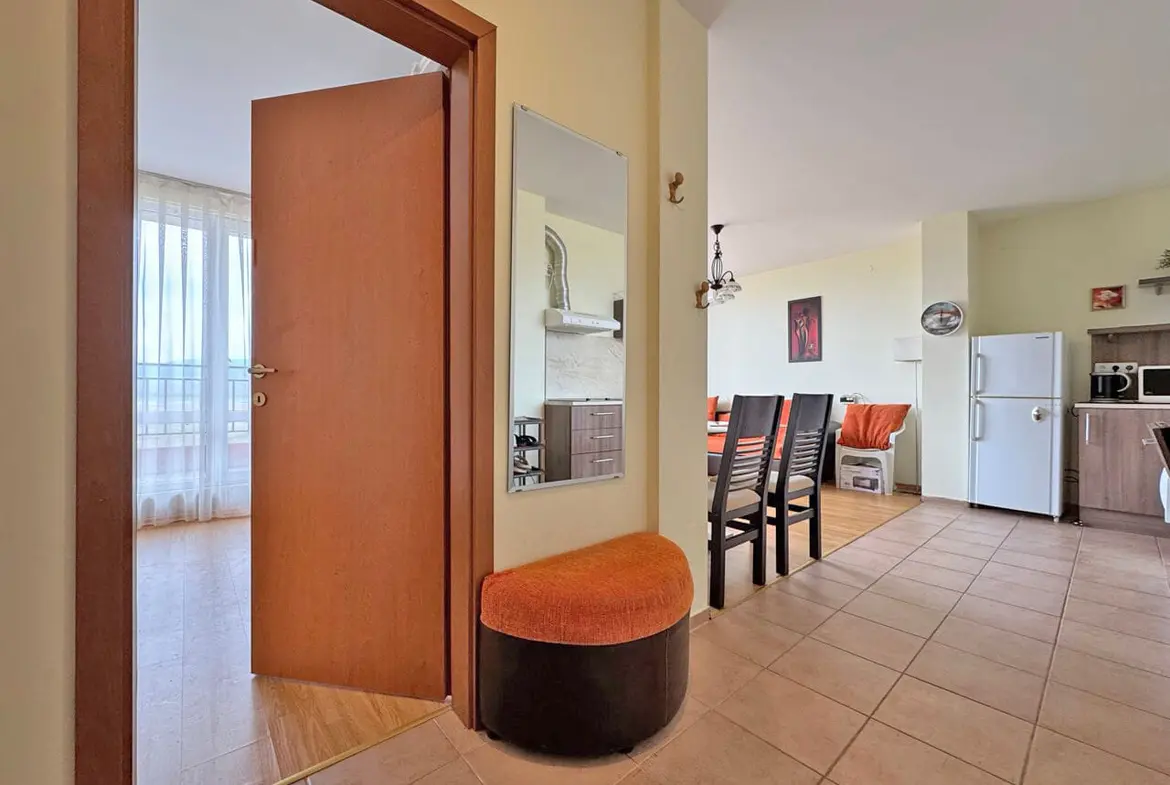 Современный интерьер квартиры с входной дверью, стулом и кухней, светлые тона и просторное помещение.