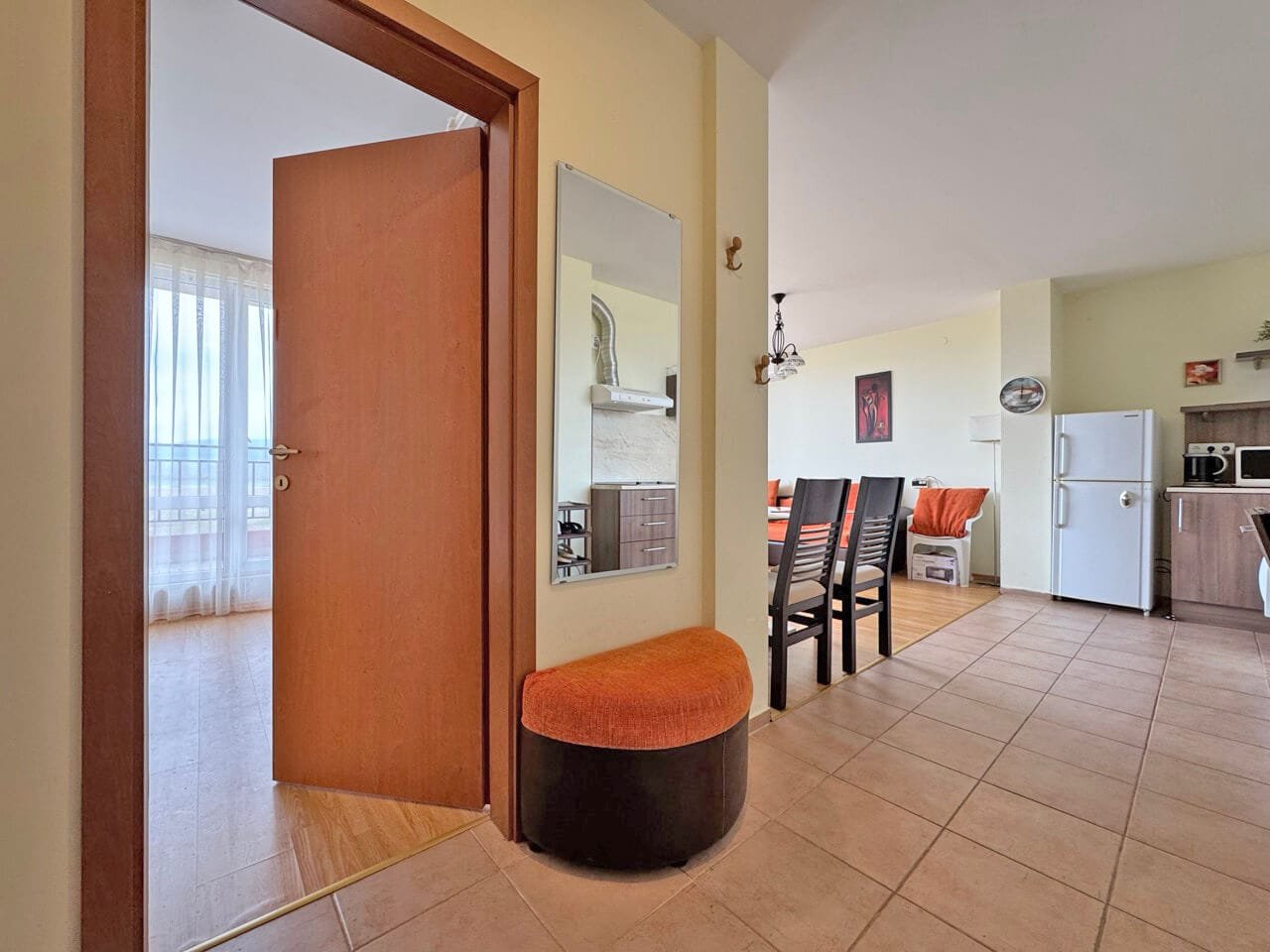 Современный интерьер квартиры с входной дверью, стулом и кухней, светлые тона и просторное помещение.