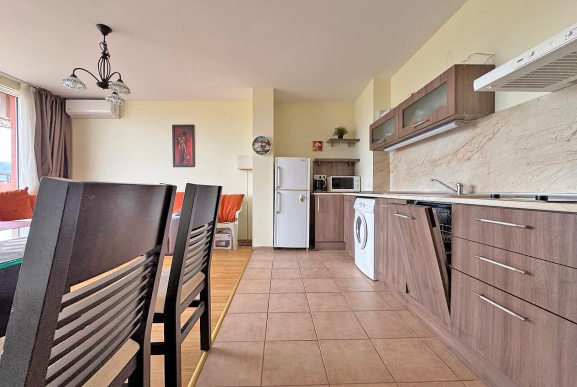 Современно оформленная кухня-гостиная с бытовой техникой, шкафами и обеденным столом, натуральное освещение от окон.