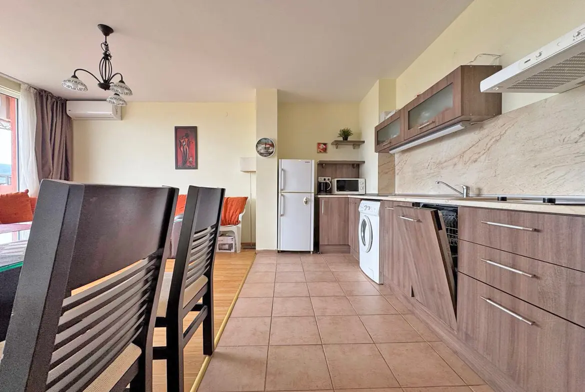 Современно оформленная кухня-гостиная с бытовой техникой, шкафами и обеденным столом, натуральное освещение от окон.