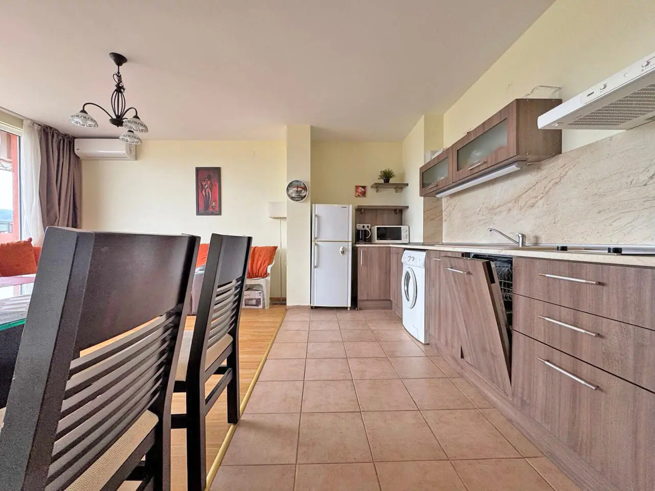 Современно оформленная кухня-гостиная с бытовой техникой, шкафами и обеденным столом, натуральное освещение от окон.