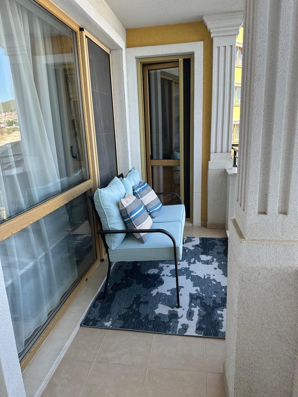 Уютный балкон с синей мебелью и декоративными подушками, идеальное место для отдыха в Болгарии.