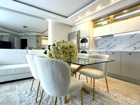 Современная кухня с белыми стульями и круглыми столом, оформленная в нейтральных тонах, с цветами на столе, противопоставляет уют и стиль.