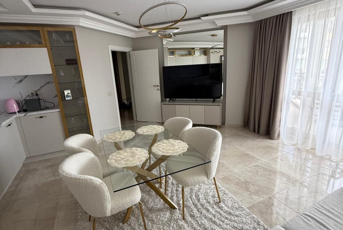 Современная квартира с стильной обстановкой, белыми креслами и стеклянным столом, подходит для покупки и аренды в Болгарии.